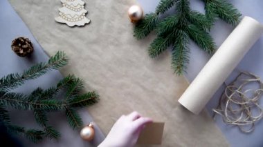Kadınların elleri Noel ve yeni yıl hediyelerini çevre dostu malzemelerle paketliyor: el işi kağıt, canlı köknar dalları, koniler, sicim, yayla bağlanmış. Doğal dekor, el yapımı, düz. Şenlik havası