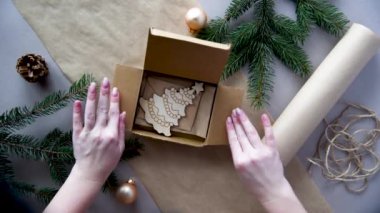 Kadınların elleri Noel ve yeni yıl hediyelerini çevre dostu malzemelerle paketliyor: el işi kağıt, canlı köknar dalları, koniler, sicim, yayla bağlanmış. Doğal dekor, el yapımı, düz. Şenlik havası