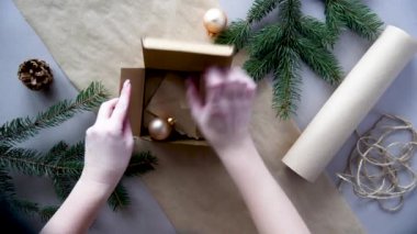 Kadınların elleri Noel ve yeni yıl hediyelerini çevre dostu malzemelerle paketliyor: el işi kağıt, canlı köknar dalları, koniler, sicim, yayla bağlanmış. Doğal dekor, el yapımı, düz. Şenlik havası