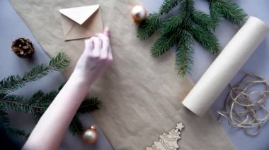 Kadınların elleri Noel ve yeni yıl hediyelerini çevre dostu malzemelerle paketliyor: el işi kağıt, canlı köknar dalları, koniler, sicim, yayla bağlanmış. Doğal dekor, el yapımı, düz. Şenlik havası