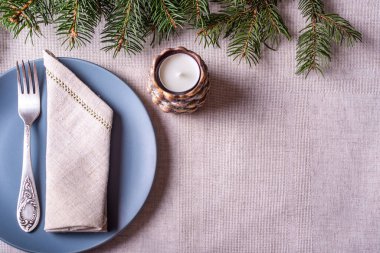 Doğal ladin kozalaklı yeşil dallar, koni şeklinde şamdanlarda beyaz mum, çatal ve gri masa örtüsü arka planda.. 