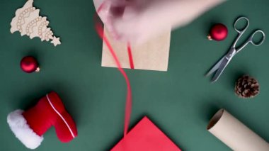 Kadın eli, Noel zamanı için hediye paketler yeşil zeminde çevre dostu malzemelerle. Kırmızı kurdele okuyla bağlanmış el işi karton kutu. Noel Baba 'nın ayakkabısı, kırmızı toplar, paket, makas..