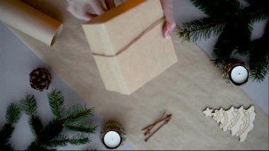 Kadınların elleri, Noel için yeni yıl hediyelerini çevre dostu malzemelerle paketliyor. Kurdele kurdelesiyle bağlanmış el işi kağıt kutu..