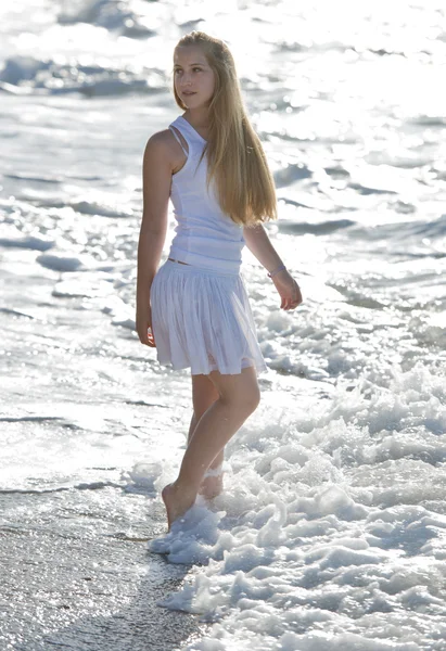 Junge Frau in weißem Kleid spaziert am Strand. — Stockfoto