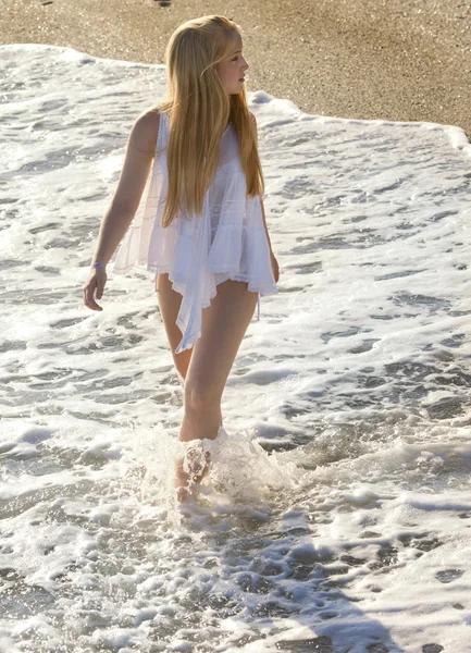 Mujer joven en vestido blanco caminando por la playa. — Foto de Stock