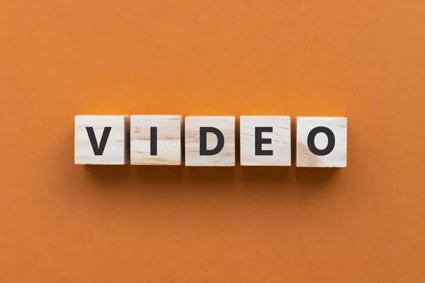 Turuncu arkaplandaki tahta küplerle ilgili VIDEO metni. Tahta bloklar. Üst manzara, düz uzanma.