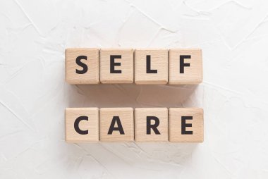 Beyaz desenli macun arkaplanındaki tahta küplere SELF CARE yaz. Kare tahta bloklar. Üst manzara, düz uzanma.