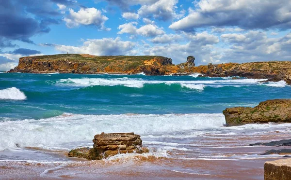 Portugal. Atlantic coast surf of atlantic Ocean with rocks, waves and foam at sand of coastline picturesque landscape panorama. Stones with green moss and blue sky with dramatic clouds.