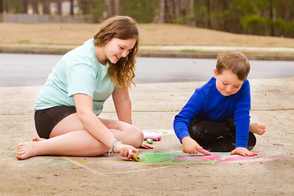 Siblings play with chalk drawing in drive way or sidewalk — Stock Photo, Image