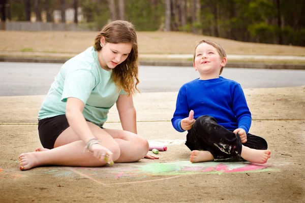 Siblings play with chalk drawing in drive way or sidewalk — Stock Photo, Image