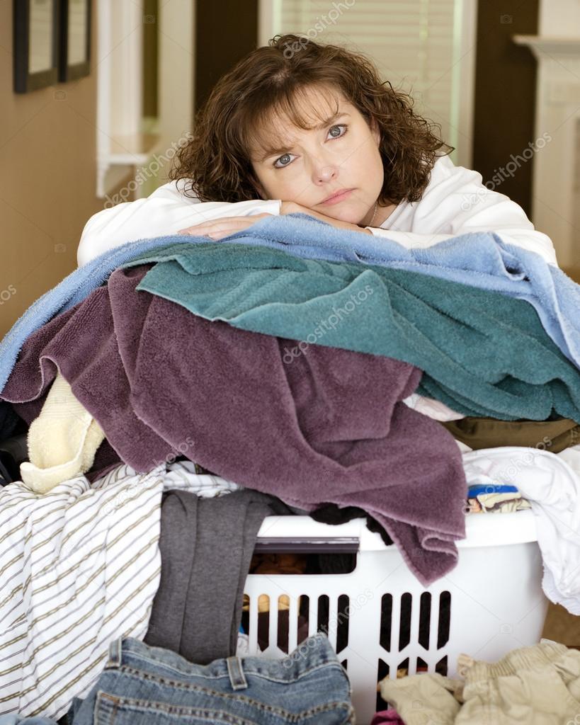 Unhappy, sad, tired woman resting on large, messy pile of laundry