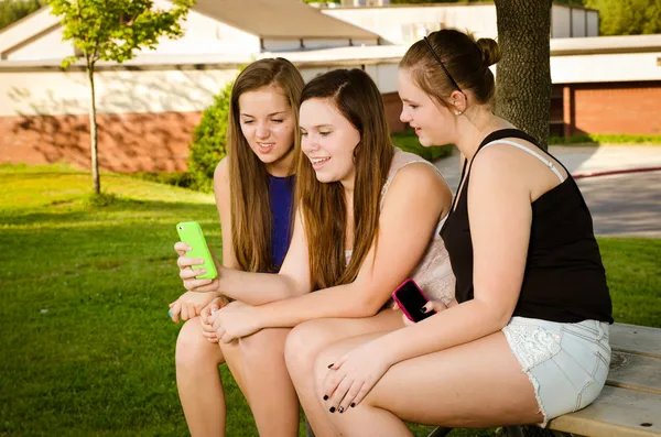 Chicas preadolescentes enviando mensajes de texto mientras pasan el rato frente a su escuela —  Fotos de Stock