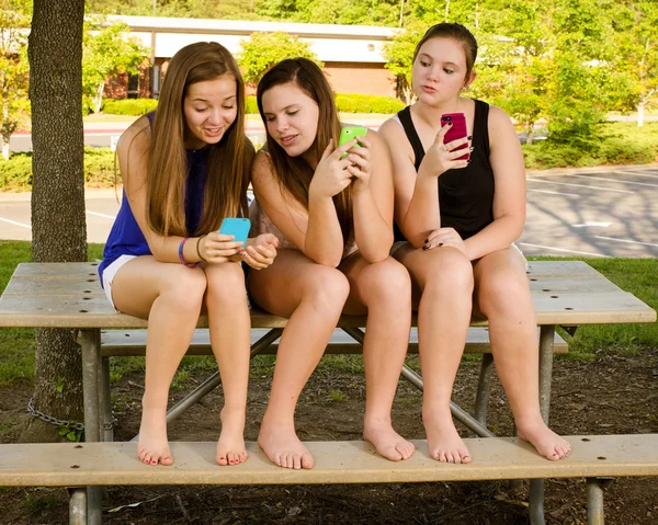 Chicas preadolescentes enviando mensajes de texto mientras pasan el rato frente a su escuela —  Fotos de Stock