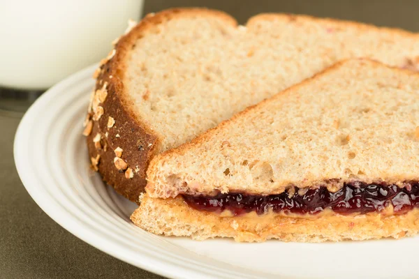 Peanut butter and jelly sandwich on wheat bread with glass of milk in background Stock Image