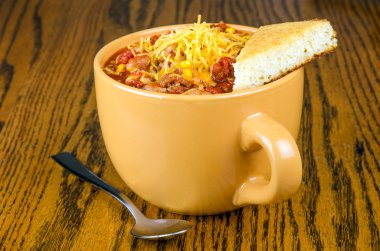 Cup of chili with cornbread and sprinkle of cheddar cheese clipart