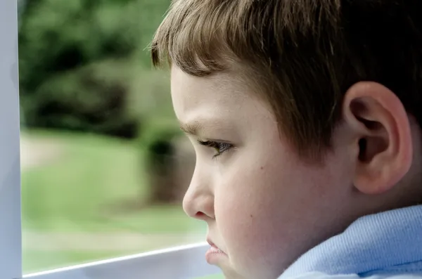 Bambino triste che guarda fuori dalla finestra in un giorno cupo — Foto Stock