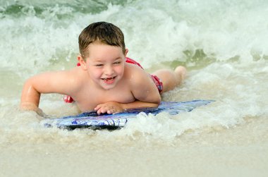 Child surfing on bodyboard at beach clipart