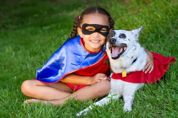 Menina de raça muito mista abraçando seu animal de estimação com ambos vestidos com fantasias de super herói — Fotografia de Stock