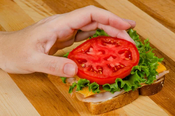 Att sätta tomat på kalkon smörgås — Stockfoto