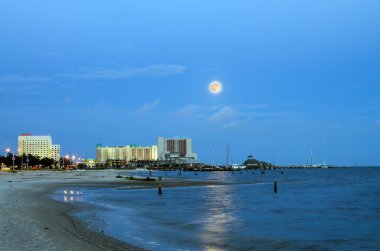 Biloxi, Mississippi, casinos and buildings along Gulf Coast shore in night time image with rising moon clipart