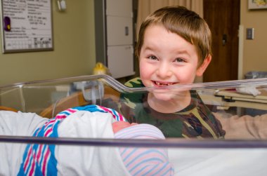 Excited boy meets his infant sibling for the first time after delivery at hospital clipart