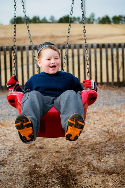 Niño feliz riendo mientras se balancea en el patio de recreo — Foto de Stock