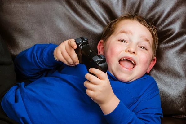 Joven niño jugando videojuego acostado en el sofá en casa —  Fotos de Stock