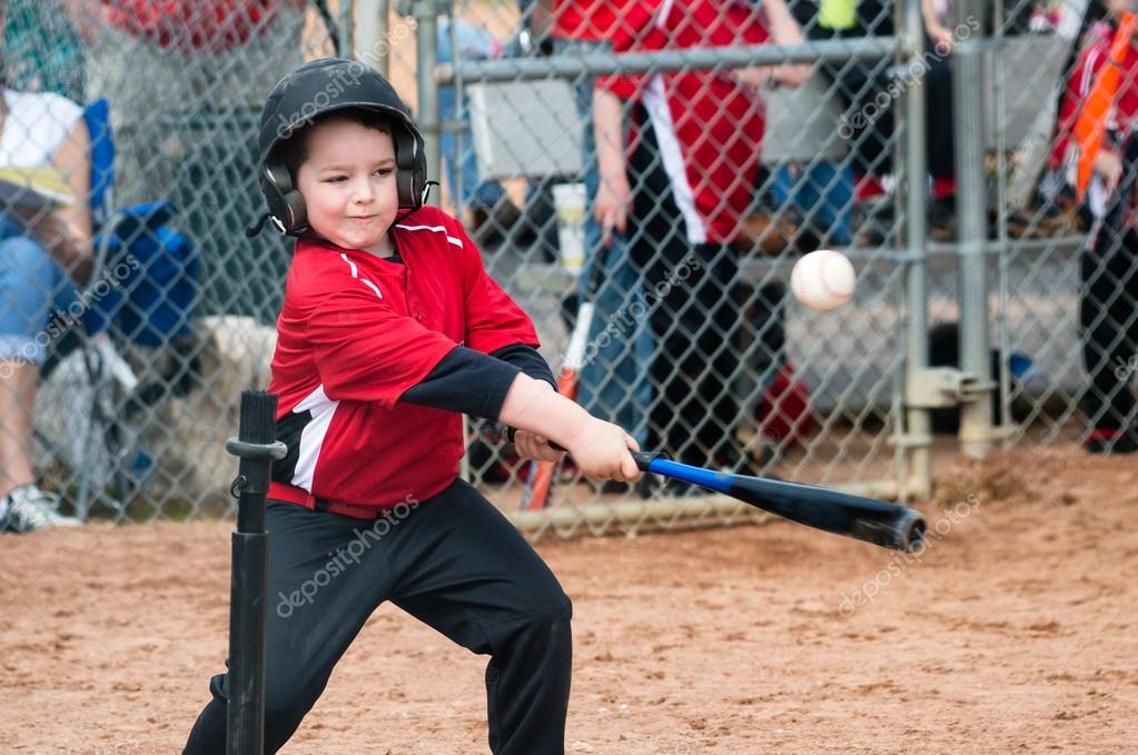 Young baseball player hitting ball off a tee during game Stock Photo by