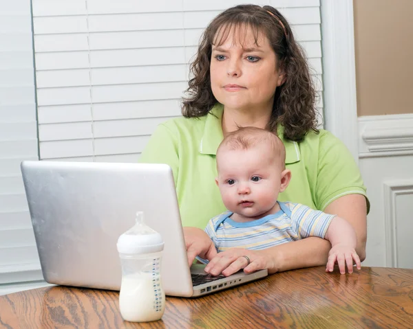 彼女のコンピューターでの作業中の持ち株の赤ちゃんを母親します。 — ストック写真