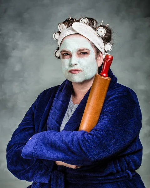 Mean and ugly housewife with facial mask, hair rollers and rolling pin — Stock Photo, Image