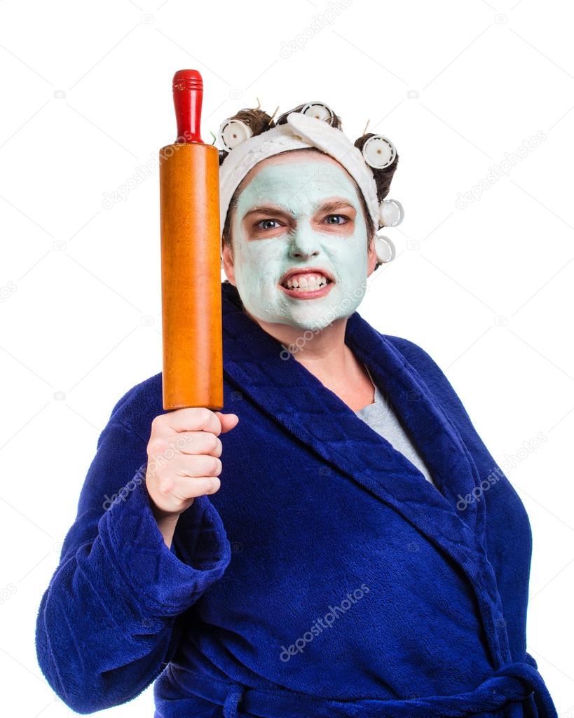 moyenne et laide femme au foyer avec masque facial, bigoudis et rouleau