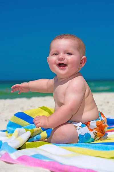 Glückliches Baby, das im Urlaub auf einem Handtuch am Strand sitzt lizenzfreie Stockbilder