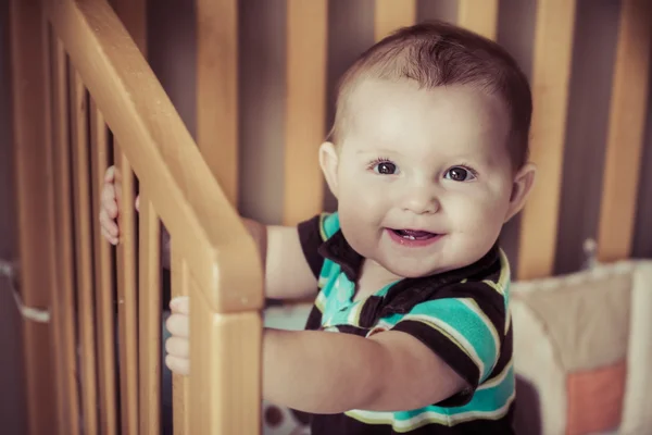 Bebê feliz em pé em seu berço na imagem com filtro vintage — Fotografia de Stock