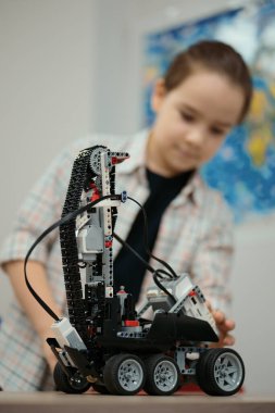 Akıllı okul çocuğu masada oturuyor ve robot bir cihaz yapıyor.