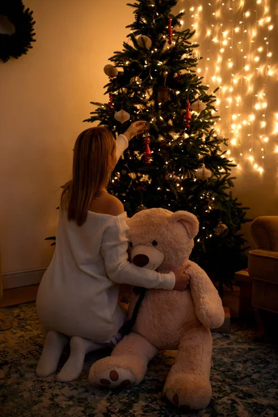 Mulher abraçando urso olhando para a árvore de Natal — Fotografia de Stock