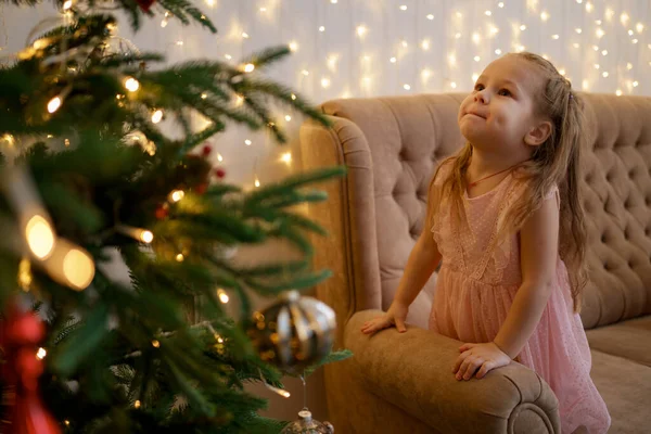 Menina bonito olhando para uma árvore de Natal, fazendo um desejo — Fotografia de Stock