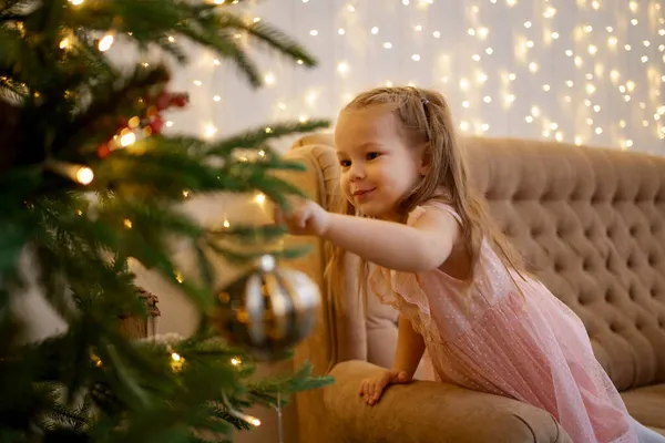 Nettes Mädchen schaut auf einen Weihnachtsbaum und wünscht sich etwas — Stockfoto