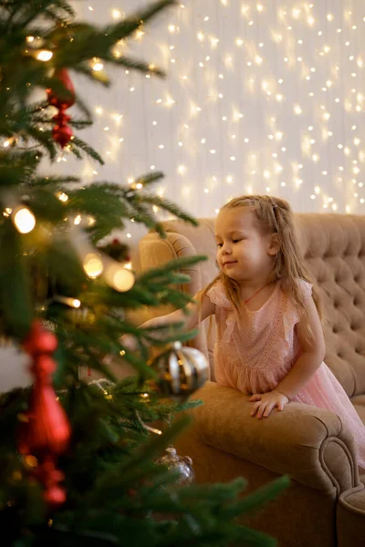 Nettes Mädchen schaut auf einen Weihnachtsbaum und wünscht sich etwas — Stockfoto