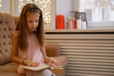 Anaokulu kızı evde kitap okuyor.
