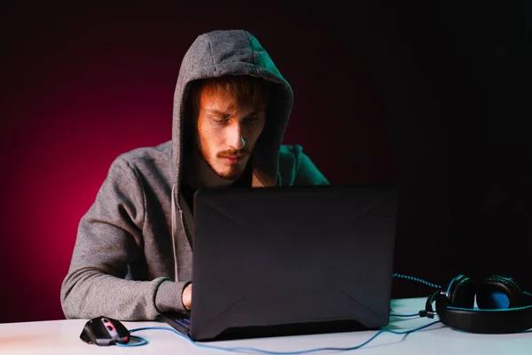 Profesionální hacker s notebookem sedět u stolu na tmavém pozadí — Stock fotografie
