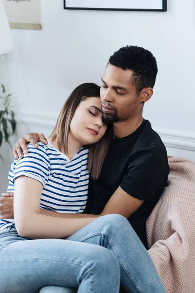 Front view of young diverse couple sitting on a armchair at home — Stock Photo, Image