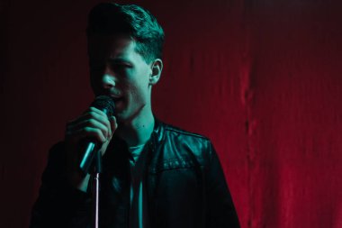 Deri ceketli bir adam kulüpte karanlık bir sahnede gösteri yapıyor.