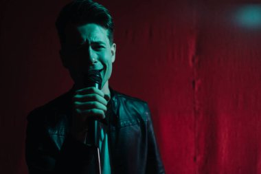 Deri ceketli bir adam kulüpte karanlık bir sahnede gösteri yapıyor.