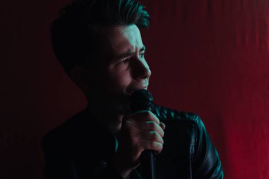 Deri ceketli bir adam kulüpte karanlık bir sahnede gösteri yapıyor.