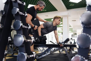 Genç adam spor salonunda kişisel antrenörle antrenman yapıyor.