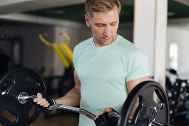 Genç çekici adam spor salonundaki kıvırcık çıtayı kaldırıyor.