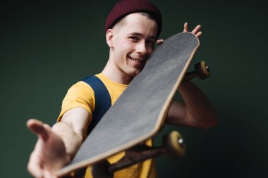 Sarı tişörtlü beyaz adam koyu yeşil arka plan duvarında paten yapıyor.