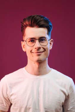 Kırmızı arka planda izole edilmiş beyaz tişörtlü, gülümseyen yakışıklı adamın yakın portresi.