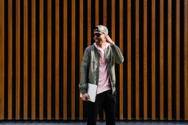 Özgüvenli genç Afro adamın portresi ahşap arka planda dizüstü bilgisayarla poz veriyor.