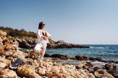Gezgin kadın deniz kıyısında yoga çalışmasının tadını çıkarıyor.